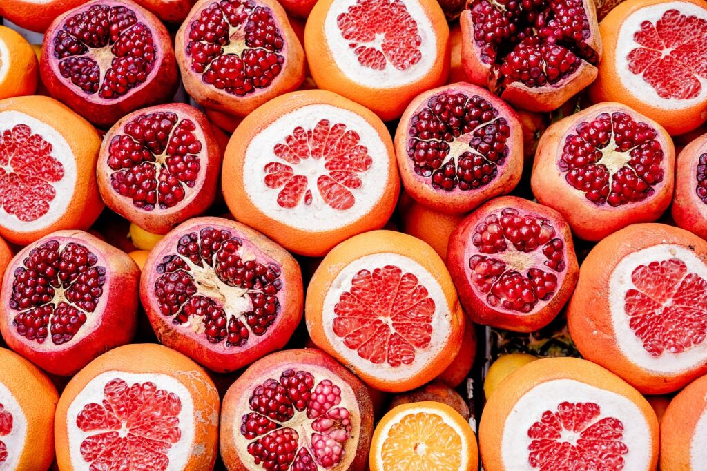 Close-up of fresh pomegranate seeds and a sliced pomegranate, highlighting the fruit's vibrant red color and nutrient-rich content, known for its antioxidants and health benefits.