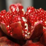 Close-up of fresh pomegranate seeds and a sliced pomegranate, highlighting the fruit's vibrant red color and nutrient-rich content, known for its antioxidants and health benefits.