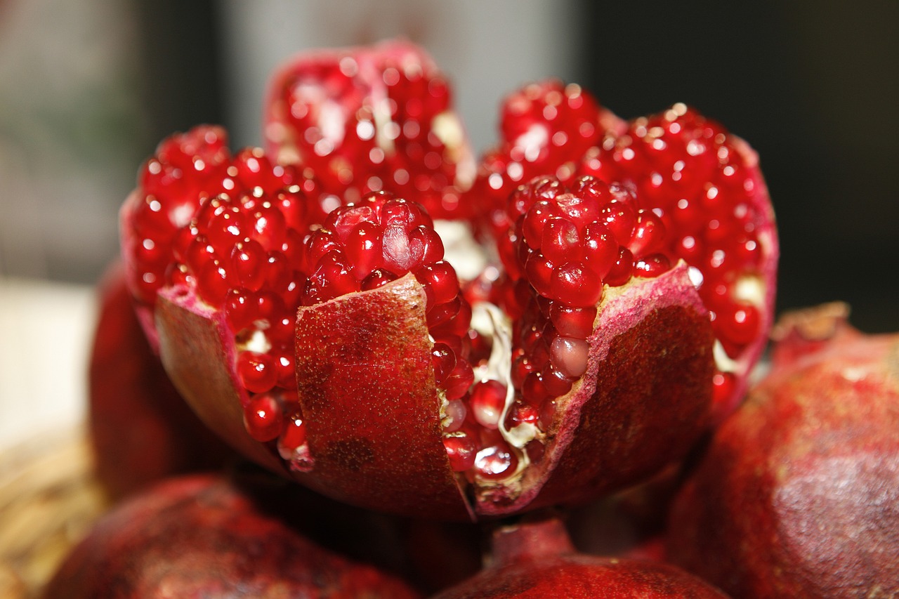 Close-up of fresh pomegranate seeds and a sliced pomegranate, highlighting the fruit's vibrant red color and nutrient-rich content, known for its antioxidants and health benefits.